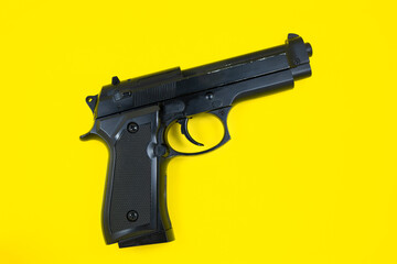 Barrel of a black gun, pistol lies on a yellow background. Close up.