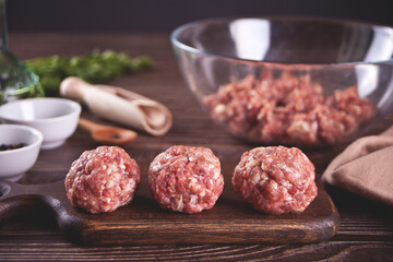 Raw meatballs on the wooden cutboard with ingredients on the background