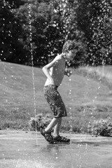 Young boy with Autism playing at a splash pad; water spray fountain outside at a playground