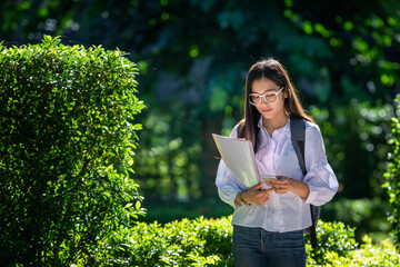 Fototapeta premium Beautiful female Asian students in trendy clothes chatting on their smartphones to plan their leisure travel. In your mobile phone, documents and notebooks, get ready to record events.