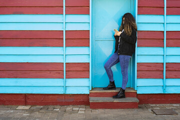 brunette woman looks at mobile phone on blue and maroon wall