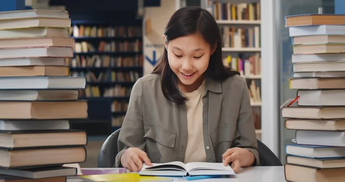 Asian school student girl reading book sitting at desk at library