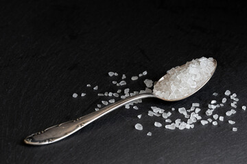 gross white sea salt on a silver spoon black background - obrazy, fototapety, plakaty