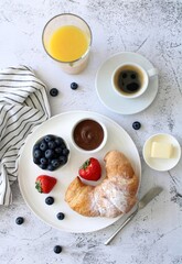 Typical French breakfast: croissant, butter, coffee with milk, juice and berries on a light background, top view.