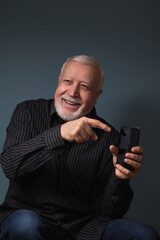 smiling charismatic elderly man shows finger at smartphone, studio shooting, portrait