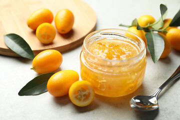 Delicious kumquat jam in jar and fresh fruits on light grey table, space for text