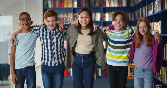 Portrait of multiethnic classmates hugging and smiling at camera in school library