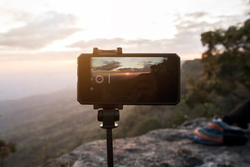 Mobile phone or smartphone on tripod with photography mode snapping a picture of sunset at the cliff : Time lapse taking sunset concept. Travel and holiday concept.