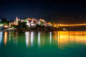 Obraz premium Spectacular illuminated panoramic cityscape of Rishikesh, the yoga capital of World located in foothills Himalayas along banks of river Ganga or Ganges in Uttarakhand state of India.