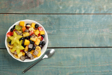 Delicious exotic fruit salad and spoon on light blue wooden table, flat lay. Space for text