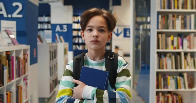 Portrait of schoolboy with backpack carrying books walking in school library
