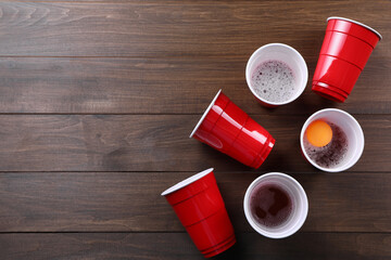 Plastic cups and ball on wooden table, flat lay with space for text. Beer pong game