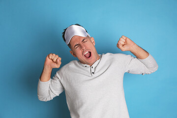 Naklejka premium Tired man with sleeping mask yawning on light blue background