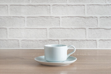 Fototapeta na wymiar White cup of coffee on wooden table in front of white brick wall