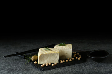 Pieces of delicious tofu with herbs, olives and soy on grey table, space for text