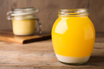 Glass jar of Ghee butter on wooden table, closeup. Space for text