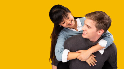 Love forever Romance young mix couple over yellow background copy space Young handsome boyfriend piggy back his cute girlfriend Happy couple wear casual sweater clothes with smile face Mix race couple