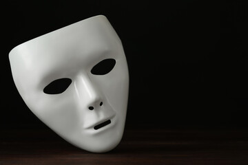 White theatre mask on wooden table against black background, space for text