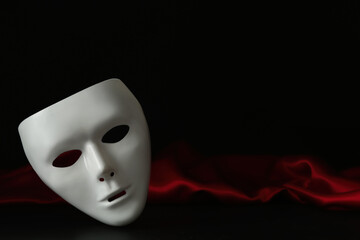 White theatre mask and red fabric on black background, space for text