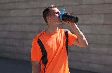 Portrait of tired young runner man drinking from a bottle the water or a protein shake, male...