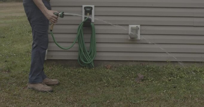 Male draining an expandable garden hose and storing it neatly on an outdoor faucet.
