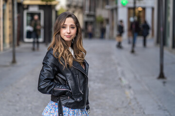 Plakat young woman with wave in hair wearing black jacket in the city