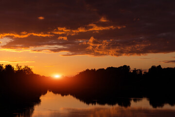 Sunset, sunrise on storm sky with dark clouds, orange yellow red sun and sunlight in reflection of river, lake water
