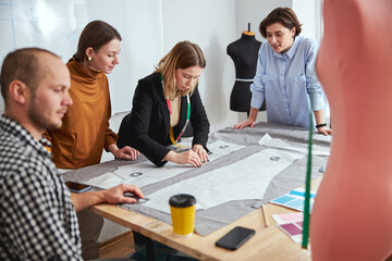 Skilled tailors watching their colleague using patterns