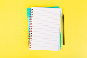 open notepad on yellow background with pencil on top, spiral notepad with blank sheet.