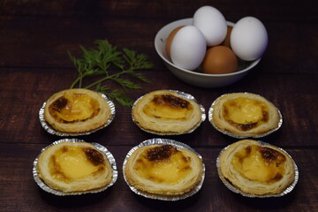 Six belem cakes on wooden board with eggs in the background