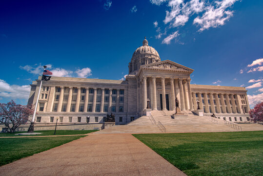 Low angle view of sidewalk leading up to the marble domed and columned Missouri state capitol building in Jefferson City in spring with blue sky.