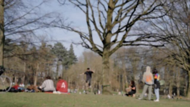 Young unrecognizable man walking and jumping on slackline between trees in the park - bokeh