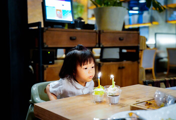 Asian baby blowing her  birthday candle on cupcake at restaurant to celebrate her birthday party.