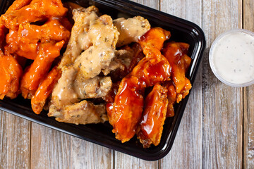 A top down view of a to-go container of assorted flavors of chicken wings.