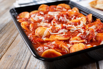 A view of a to-go container of ravioli in marinara sauce.