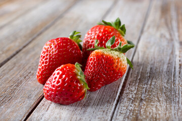 A view of four strawberries in a group, on a wood table surface.