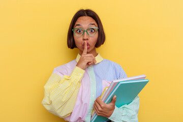 Young mixed race student woman isolated on yellow background keeping a secret or asking for silence.