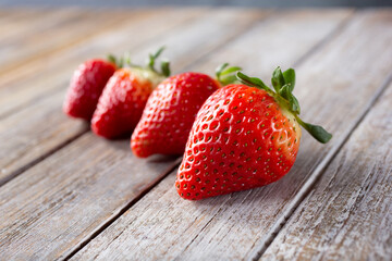 A view of four strawberries in a row, on a wood table surface.