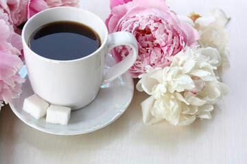 White cup with coffee and delicate peony flowers.