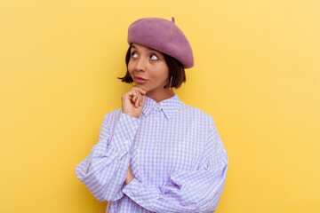 Young mixed race woman wearing a beret isolated on yellow background looking sideways with doubtful and skeptical expression.