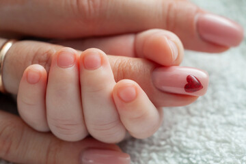 Infant holding mommy's finger. Mum taking care of the infant baby. Heart sign on mom's nail. Family, motherhood, love concept.