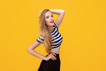 Obraz premium Shy girl smiling looking to the camera. Caucasian charming girl with long hair wearing stripped t-shirt, standing against yellow studio background having fun