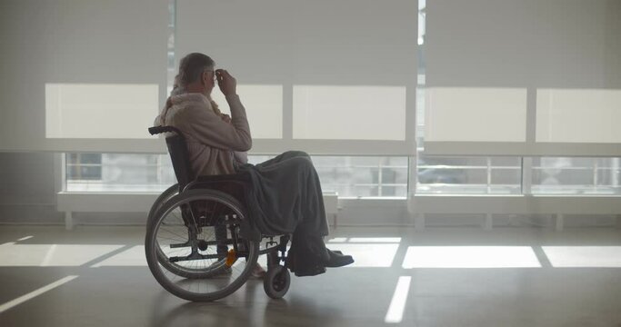 Preteen girl visiting grandfather in wheelchair at hospital corridor