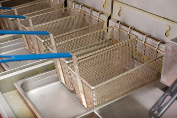 A view of a row of empty fry baskets hanging on a deep fryer appliance, in a restaurant kitchen setting.
