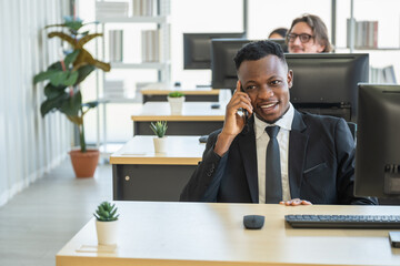 Diversity Business and Work palce concept. African businessman talking on call with mobile smartphone in office with desktop computer.