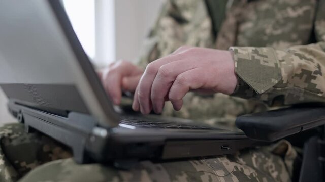 Close-up of male hands of military man typing on laptop keyboard. Unrecognizable Caucasian soldier or veteran texting messaging online indoors. Modern technologies and wireless communication