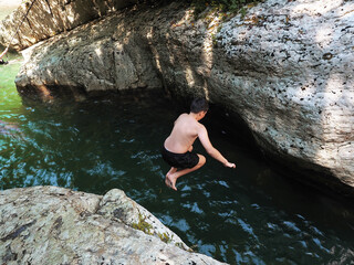 A boy in black swimming trunks jumped from a canyon into an emerald river