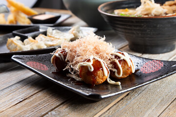 A view of a plate of takoyaki among other Japanese appetizers on a table.