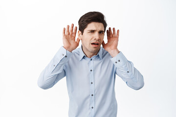 What I cant hear you. Confused male office manager, holding hands near ears and looking puzzled,...