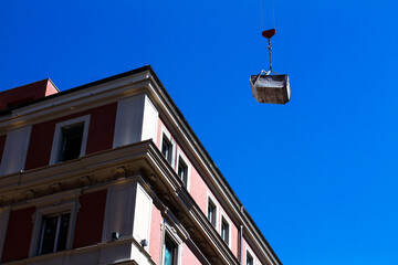 Fototapeta na wymiar Renovation works in a residential area of ​​Rome, a crane transports cargo, residential buildings and blue sky.